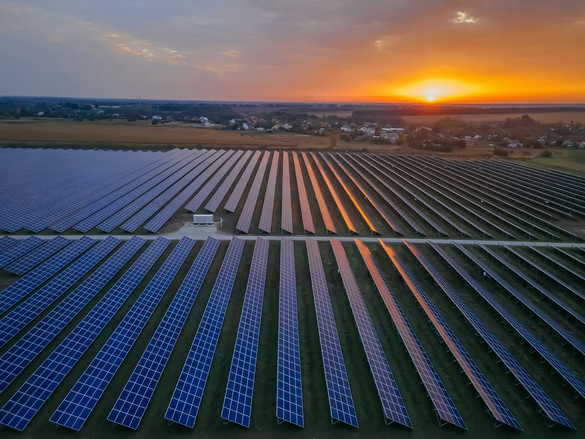 Aerial drone view into large solar panels at a solar farm at bright sunset. Solar cell power plants.